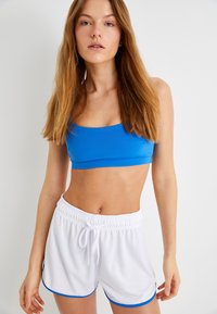 Blå sportstopp med kort längd, i kombination med vita shorts med dragsko och blåa detaljer. Slät textur med en åtsittande design.