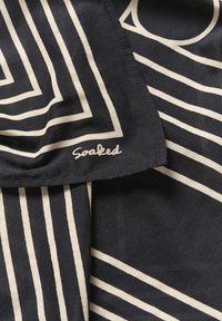 Bomuldsstof med en sort baggrund, prydet med kraftige hvide geometriske linjer og ordet "Soaked" skrevet i kursiv ved den nederste kant.