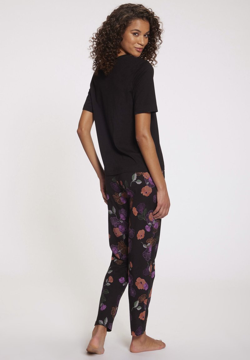Top negro de manga corta combinado con pantalones ajustados que presentan un colorido patrón floral sobre un fondo oscuro. Tejido suave y ligero.