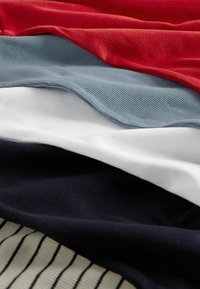 Baumwollstofflagen in Rot, Grau, Weiß und Marineblau, mit strukturierten Oberflächen und subtilen Rippungen; ein gestreiftes Muster auf der untersten Lage.