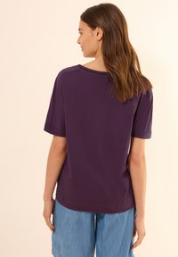 Camiseta corta de manga en color púrpura, hecha de algodón suave, que presenta un corte holgado y un escote redondeado, combinada con pantalones cortos de mezclilla azul.