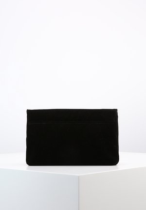 Czarna prostokątna kopertówka o miękkiej, materiałowej fakturze, stojąca pionowo na białym sześciokątnym podeście na tle gładkiego białego tła.