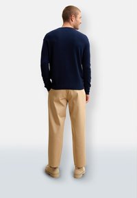 Maglione blu navy abbinato a pantaloni beige chiaro. Il maglione ha maniche lunghe e un colletto rotondo; i pantaloni hanno una vestibilità comoda.