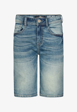 Valkoinen puuvillainen poolopaita, jossa rintalogo, yhdistetty käännettyihin farkkushortseihin. Malli käyttää valkoisia tennareita ja nilkkasukat. Neutraali tausta.