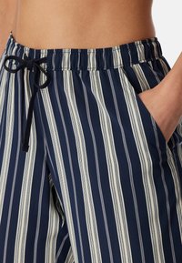 Dunkelblaue gestreifte Hosen mit elastischem Bund, Kordelzug und seitlichen Taschen. Vertikale cremefarbene Streifen setzen einen Kontrast zum Design.