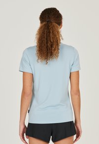Lysblå kortærmet t-shirt lavet af glat stof, med et enkelt design og en lige pasform. Sorte shorts synlige ved kanten.