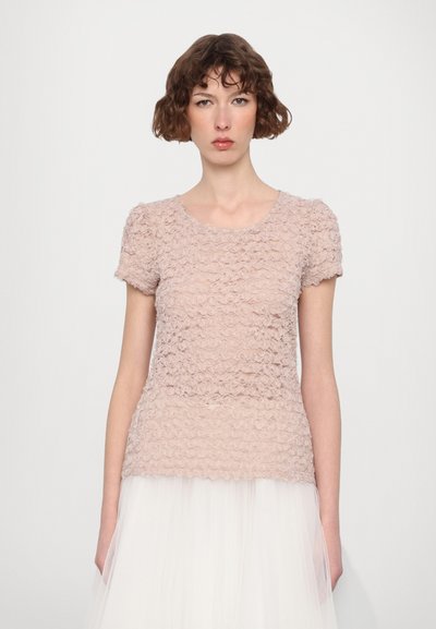 T-shirt à manches courtes en tissu doux et texturé de couleur rose clair, avec un motif ondulé et volé, associé à une jupe en tulle blanc à multiples couches.