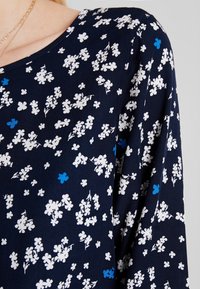 Marineblauer Stoff mit kleinen weißen und blauen Blumenmustern, der eine weiche Textur und einen runden Ausschnitt aufweist. Das Design umfasst kurze Ärmel.