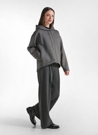Overmaatse hoodie in glad grijs stof, gecombineerd met brede gestreepte broeken. Glanzende zwarte schoenen maken de outfit compleet.