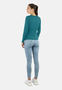 Türkiser Langarm-Top, taillierte Passform, kombiniert mit hellen Jeans und weißen Sneakers. Glatte Textur, einfacher Rundhalsausschnitt, minimale Details.