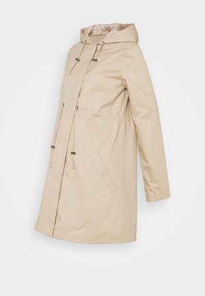 Beige damesmantel van middellange lengte met capuchon, verstelbare trekkoorden bij de capuchon en taille, en schuine voorzakken.