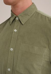 Camicia in corduroy verde oliva con colletto button-down, pattina centrale con bottoni e taschino sul petto con dettagli di cucitura visibili.