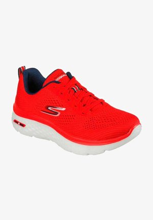 Zapatilla deportiva roja con parte superior de malla, suela blanca y superficie texturizada. Cuenta con cordones y un cuello en contraste de color azul marino.