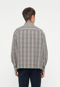 Plaid shirt in brown, white, and gray tones, featuring a buttoned collar, long sleeves, and a slightly loose fit. Visible back seam details.