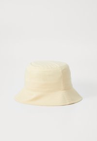 Bucket-hatt i lys beige stoff med rund krone og vid, nedovervendt skjerm. Glatt tekstur med sydd detaljer rundt kronen.