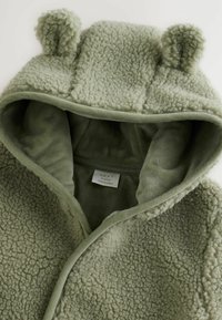 Fleece hooded jacket in soft green with bear ears, textured outer layer, smooth inner lining, and a front closure. Label visible inside.