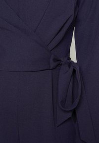 Knytklänning i mörk marinblå crepe, med långa ärmar, knyt i midjan och en silkeslen yta med en subtil lyster.