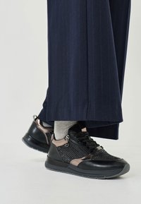 Baskets noires et grises avec des sections en maille, des accents texturés lisses et un détail zippé. Associées à des chaussettes grises et un pantalon à rayures navy.