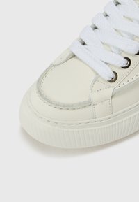 Sneaker bianca in pelle con suola in gomma testurizzata, punta tonda e lacci piatti bianchi. Presenta occhielli in metallo e accenti cuciti lungo le cuciture.