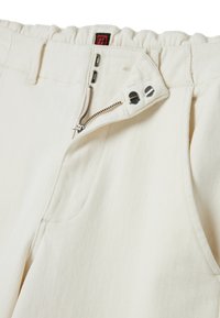 Pantalones color crema con un corte relajado, que cuentan con una cinturilla fruncida, cremallera de metal y bolsillos delanteros con sutiles detalles de costura.