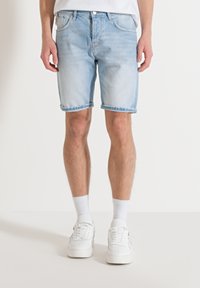 Pantalones cortos de mezclilla azul claro con un lavado ligeramente desgastado, diseño de cinco bolsillos y dobladillos enrollados. Combinados con zapatillas blancas y calcetines de longitud hasta el tobillo.
