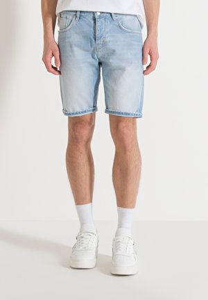 Pantalones cortos de mezclilla azul claro con un lavado ligeramente desgastado, diseño de cinco bolsillos y dobladillos enrollados. Combinados con zapatillas blancas y calcetines de longitud hasta el tobillo.