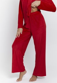 Rode loungewear set, bestaande uit een langwerpige top en wijde broekspijpen. Stof heeft een geribbelde textuur, met een ontspannen pasvorm en een elastische tailleband.