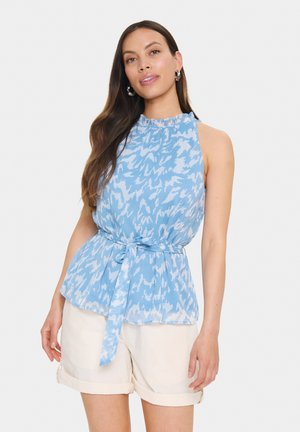 Blouse sans manches de couleur bleu clair avec un col à volants, coupe ample et taille nouée. Présente un motif abstrait subtil dans des nuances de bleu.