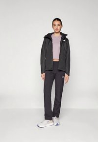 Czarna wodoodporna kurtka z kapturem, zestawiona z czarnymi spodniami i szarymi trampkami. Strój uzupełnia dopasowany, jasnofioletowy top.