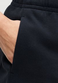 Tissu texturé bleu marine avec une poche latérale dans laquelle une main est glissée, mettant en valeur une finition lisse et un motif de tissage subtil.