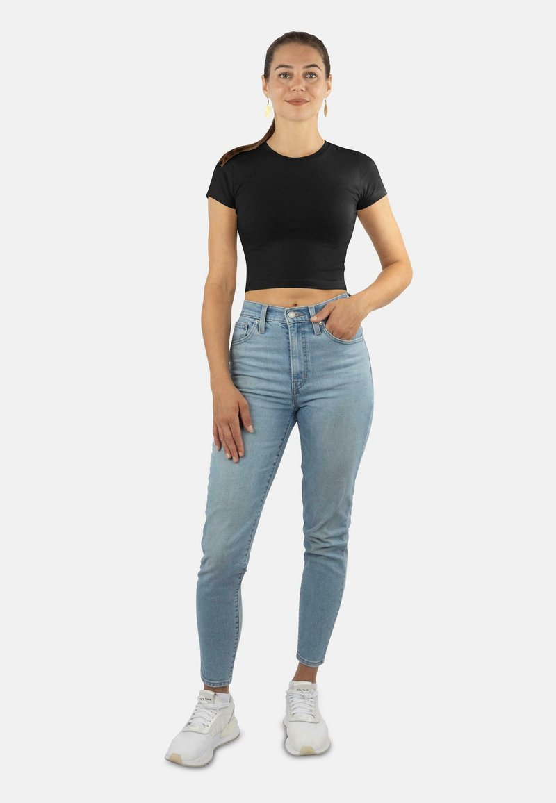 Schwarzes cropped T-Shirt mit kurzen Ärmeln, kombiniert mit hellblauen, hochgeschnittenen Skinny Jeans und weißen Sneakers. Einfaches Design, glatte Textur.