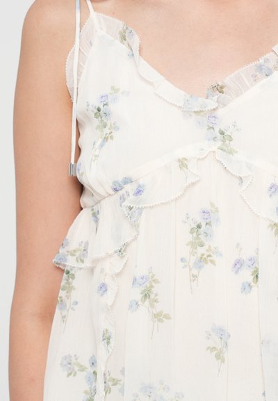 Top din țesătură ivory cu model floral, cu accente volănașe, bretele subțiri și detalii delicate cu flori albastre și verzi pe toată suprafața.