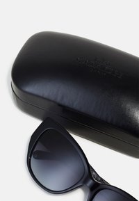 Schwarzes Leder-Sonnenbrillenetui mit eingeprägtem "COACH"-Logo. Schwarze Sonnenbrille mit kantiger Form und dunklen, verlaufsförmigen Gläsern.