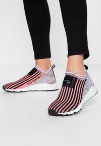 Stickade sneakers i rosa och svart med vertikala ränder. Har en slip-on design, texturerad ovandel och vit gummisula med bra grepp.