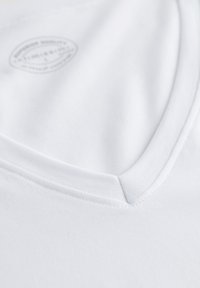 Biała bawełniana koszulka typu V-neck o gładkiej fakturze. Posiada szyty dekolt i małą wdrukowaną metkę w pobliżu kołnierza.