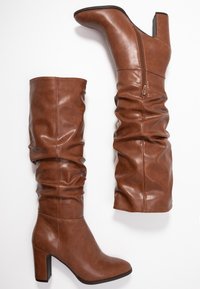 Botas de cuero marrón hasta la rodilla con un diseño holgado, que cuentan con un cierre de cremallera en un lado y un tacón grueso. Textura suave con un acabado brillante.