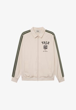 Casaco bege com fecho éclair, mangas com riscas verdes, logo "YALE" e gráfico de bulldog. Apresenta bolsos laterais e punhos canelados. Tecido suave.