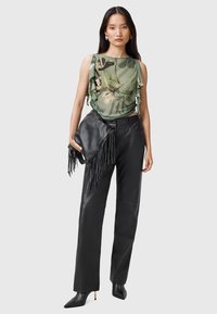 Top floreale verde con dettagli a volant, abbinato a pantaloni larghi in pelle nera e una pochette in pelle con frange. Tacchi neri a punta completano il look.