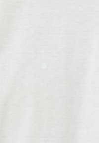 Lys grå t-shirt stof med en blød tekstur, der har en lille hvid prikdetalje i midten. Nærbillede der fremhæver materiale og design.