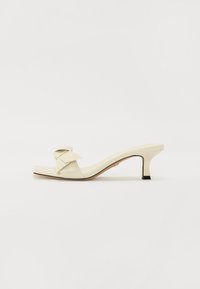 Cream-colored heeled sandal with a square toe, bow accent on the strap, and a slanted 5 cm heel featuring a black base.