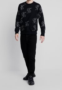 Felpa nera con motivo logo CK in grigio, colletto a giro, maniche lunghe, polsini a costine, abbinata a jeans neri e sneaker nere.
