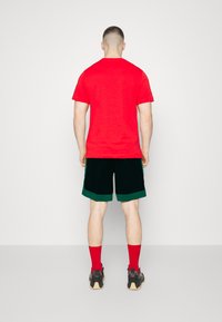 Rød bomulds t-shirt, grøn og sort shorts, røde sokker og sorte sneakers. Simpelt design, mellemlang pasform og ensfarvet farveskema.