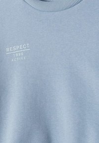 Sweatshirt bleu clair avec un col rond côtelé. Texte blanc imprimé sur le devant avec "RESPECT", "1996" et "ACTIVE". Texture douce.