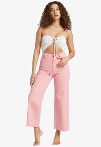 Top bandeau bianco a coste con un nodo centrale e design con ritagli, abbinato a jeans a vita alta, larghi e di colore rosa chiaro con orlo grezzo.