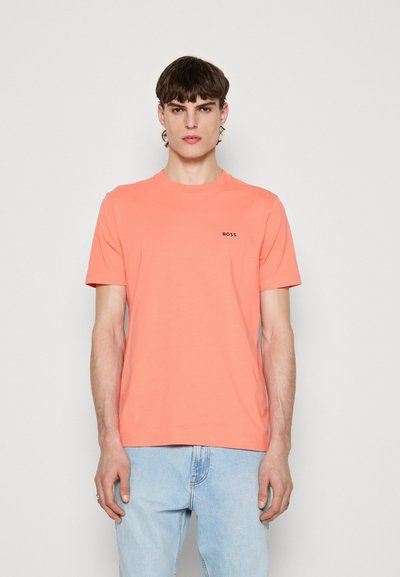 T-shirt en coton corail avec col rond et manches courtes, présentant un petit logo noir "BOSS" sur la poitrine. Porté avec un jeans bleu clair.