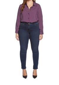 Fialovo-bíle pruhovaná dlouhá košile s knoflíky, doplněná tmavě modrými skinny džíny a černými lodičkami na vysokém podpatku.