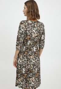 Ziedu kleita ar trīs ceturtdaļu piedurknēm, zaļā, brūnā un baltā krāsā, ar pieguļošu jostasvietu un plūstošu svārku ar smalku spīdumu.