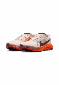 Et par beige og orange Nike ZoomX løbesko med maroon swoosh-logoer og Vibram såler vinkles til højre på hvid baggrund.