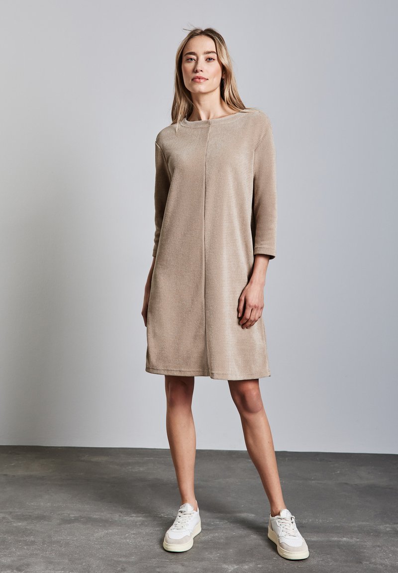 Robe beige longueur genoux en tissu texturé, décolleté rond, manches trois-quarts et coupe droite. Associée à des baskets blanches.