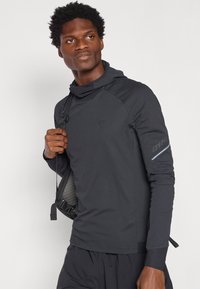 Tricou cu mânecă lungă și glugă, de culoare neagră, confecționat dintr-un material texturat și cu cusături plate. Are un șnur de ajustare pe umăr și accente reflectorizante pe mânecă.